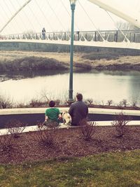 Rear view of people sitting on bench by bridge