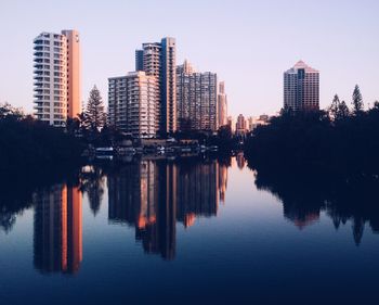 Reflection of trees and buildings in lake against sky in city