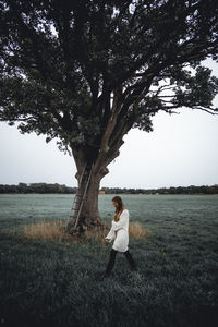 Woman standing by tree on field against sky