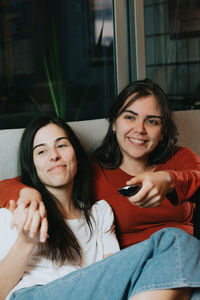 Smiling lesbian couple watching movie while sitting on sofa