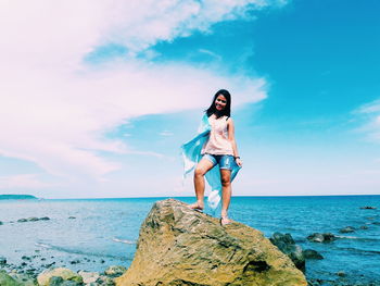 Smiling young woman standing on rock against sea