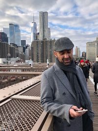 Young man using mobile phone in city against sky during winter