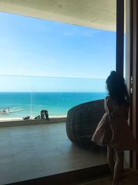 Rear view of woman looking at sea through window