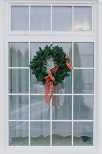 Christmas wreath with a red bow on a white window in a private house