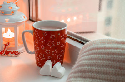 Winter still life with mug with hot drink, two marshmallow, candle on window. valentine concept. 