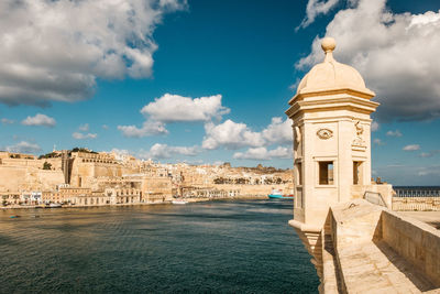 Historical buildings and sea against cloudy sky