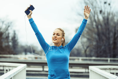 Portrait of smiling young woman using mobile phone against sky