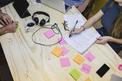 High angle view of young woman writing in book at wooden desk in office