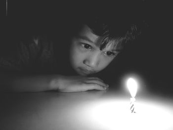 Cute boy looking at illuminated candle in dark