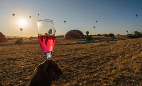 Man holding glass of field against sky during sunset