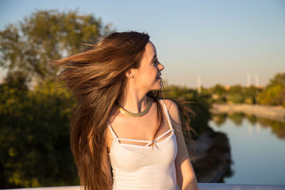 Young woman with tousled hair standing by railing over river