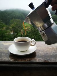 Close-up of coffee cup on table with a view of forrest behind. 