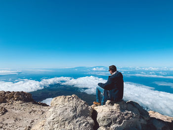 Man sitting on rock against blue sky