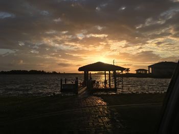 Silhouette gazebo by lake against sky during sunset