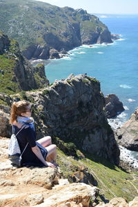 Woman sitting on rock by sea against sky