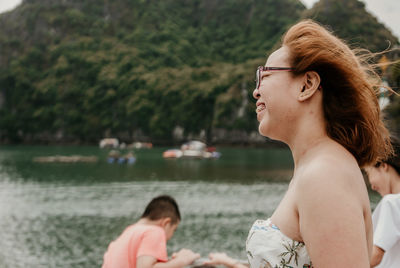 Side view of smiling young woman standing by lake against mountain