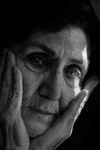 Close-up portrait of senior man with hands on chin against black background