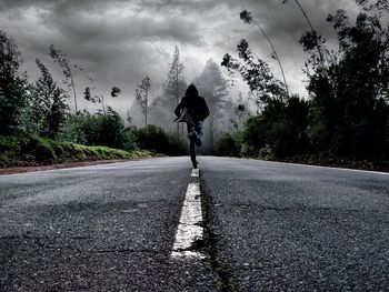 Rear view of man running on road against cloudy sky