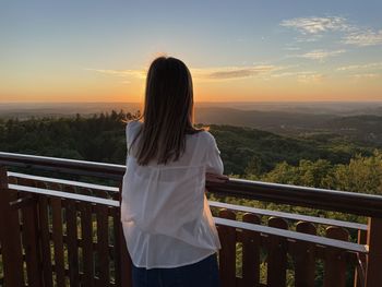 Rear view of woman standing against sky during sunset