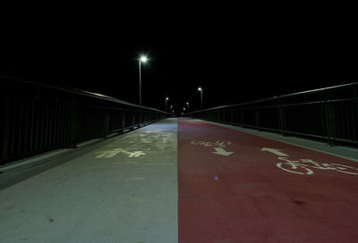 Illuminated street lights on road against sky at night