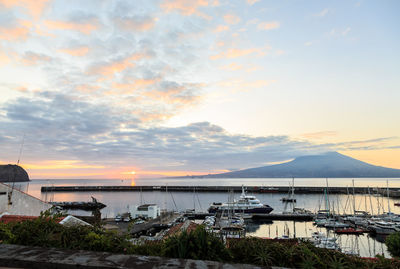 Boats moored in harbor at sunset