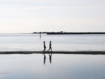 Silhouette friends standing on beach against sky