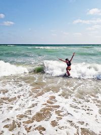 Woman with arms raised standing in sea against sky