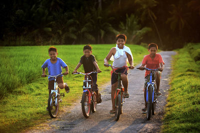 Four boys riding bicycles on dirt road at field