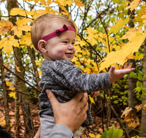 Cropped hands of father lifting daughter in forest during autumn