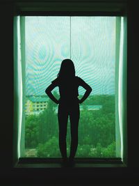 Silhouette woman standing by glass window with hands on hip