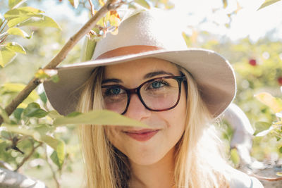 Portrait of smiling young woman wearing eyeglasses and hat by plants