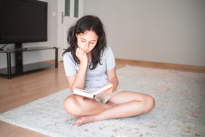 Young woman using mobile phone while sitting on floor at home