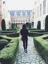 Rear view of woman walking on pathway at garden by building