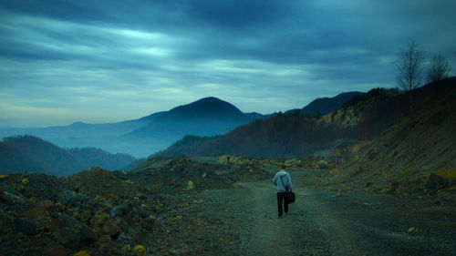 Rear view of man walking on mountain against sky