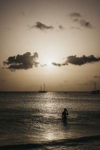 Silhouette person in sea against sky at dusk