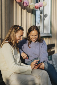 Woman sharing smart phone with female friend sitting during dinner party at cafe