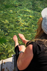 Mature woman sitting on dock splashing bare legs in lake