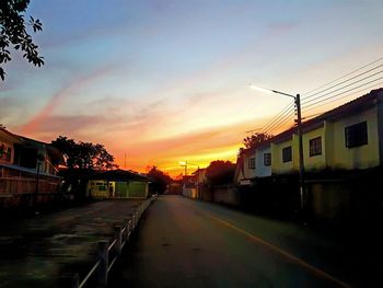 Road amidst buildings against sky during sunset