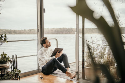 Man using mobile phone while sitting on window