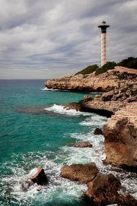 Lighthouse on rocks by sea against sky