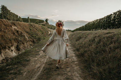 Rear view of woman walking on field against sky