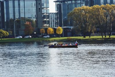 People on river by trees in city