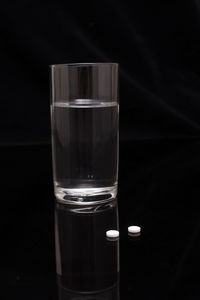 Close-up of water in glass by pills on table