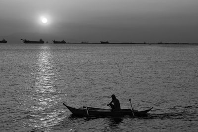 Silhouette people in boat in sea against sky during sunset