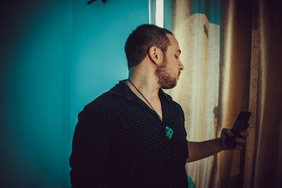 Young man using smart phone while standing against wall