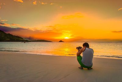 Woman sitting on beach against sky during sunset