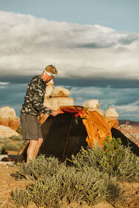 Man in camo jacket sets up tent at sunset in the desert of utah