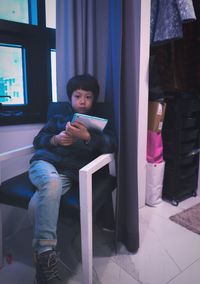 Full length of boy holding digital tablet while sitting on chair at home