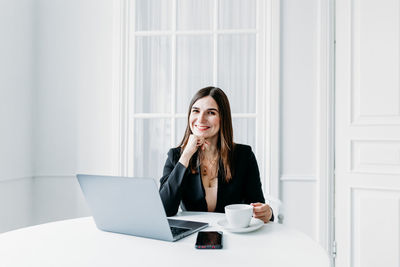 Portrait of young woman using phone while sitting on table