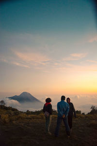 Rear view of men standing on mountain against sky during sunset